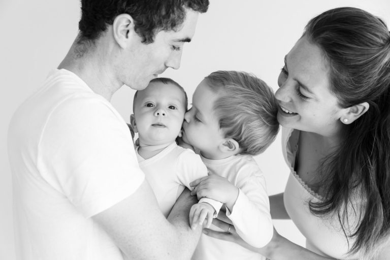 portrait de bébé en noir et blanc, entouré de sa famille et de son grand frère qui l'embrasse