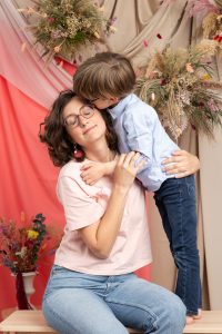 photo d'un enfant faisant un petit bisou à sa maman (Lucille) dans un décor fleuri beige et rosé